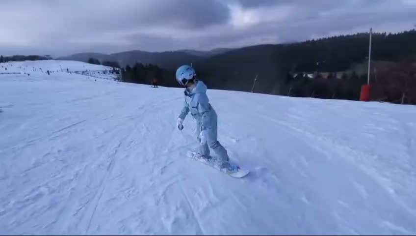 Une élève en snowboard enchaîne ses virages sur une piste